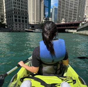 Me in a kayak on a solo date, picture taken from behind me facing some buildings in Chicago. I am on the Chicago River.