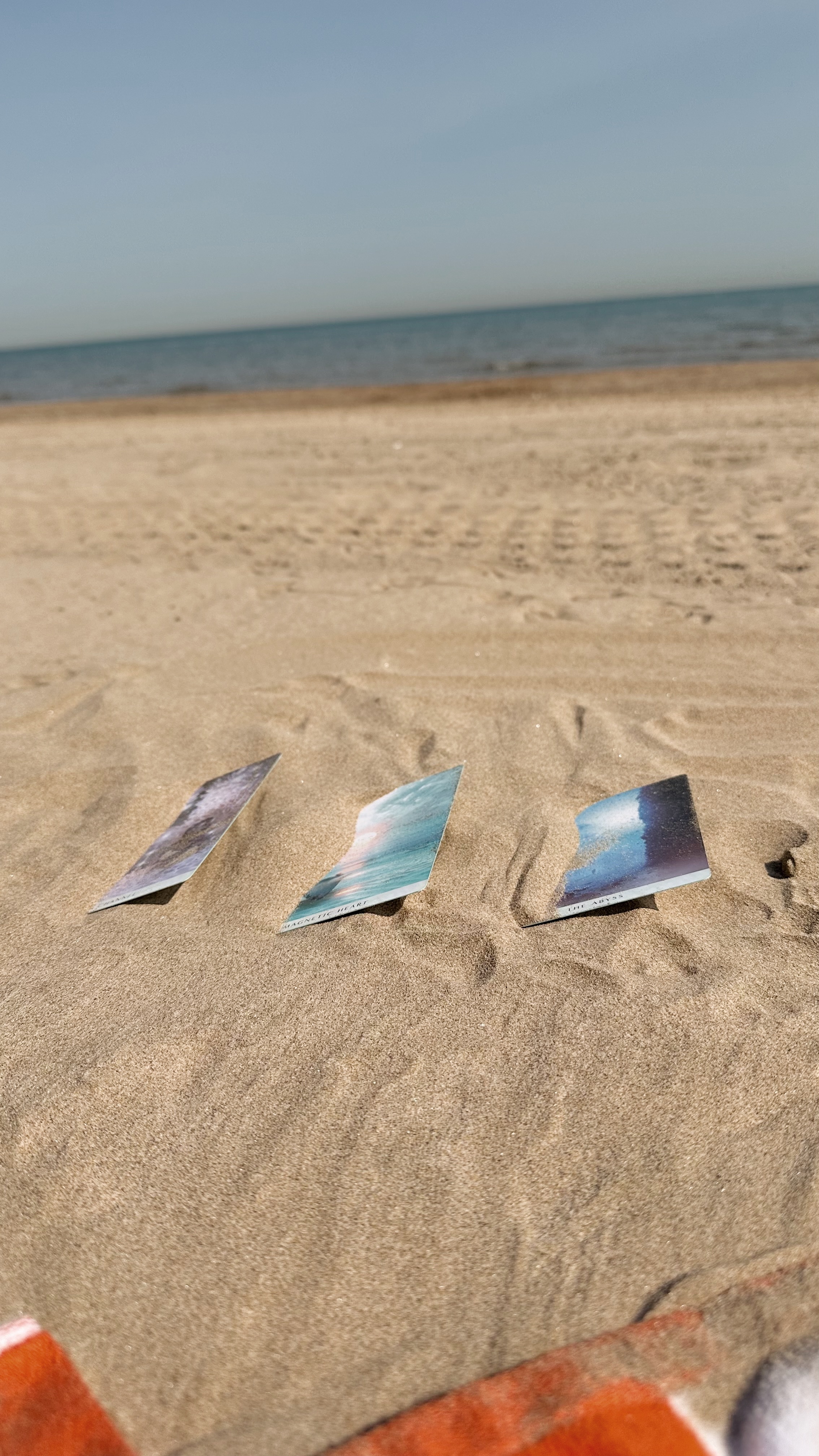 three oracle cards in the sand on the beach. This is how i keep them from flying away during my autumn equinox ritual...