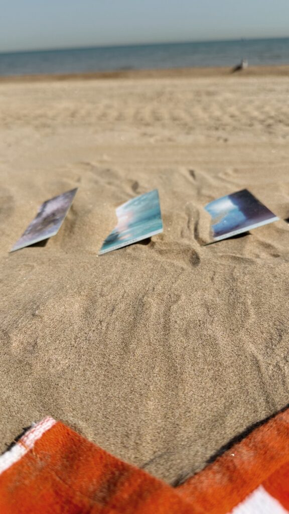 Three oracle cards wedged into the sand to avoid blowing away at the bach.